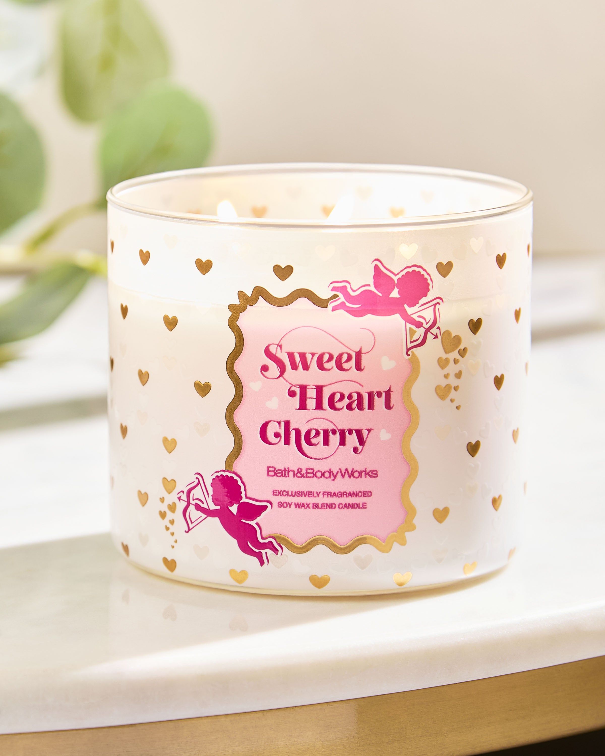 Svíčka Sweet Heart Cherry s růžovým logem a zlatými srdíčky na světlém povrchu.