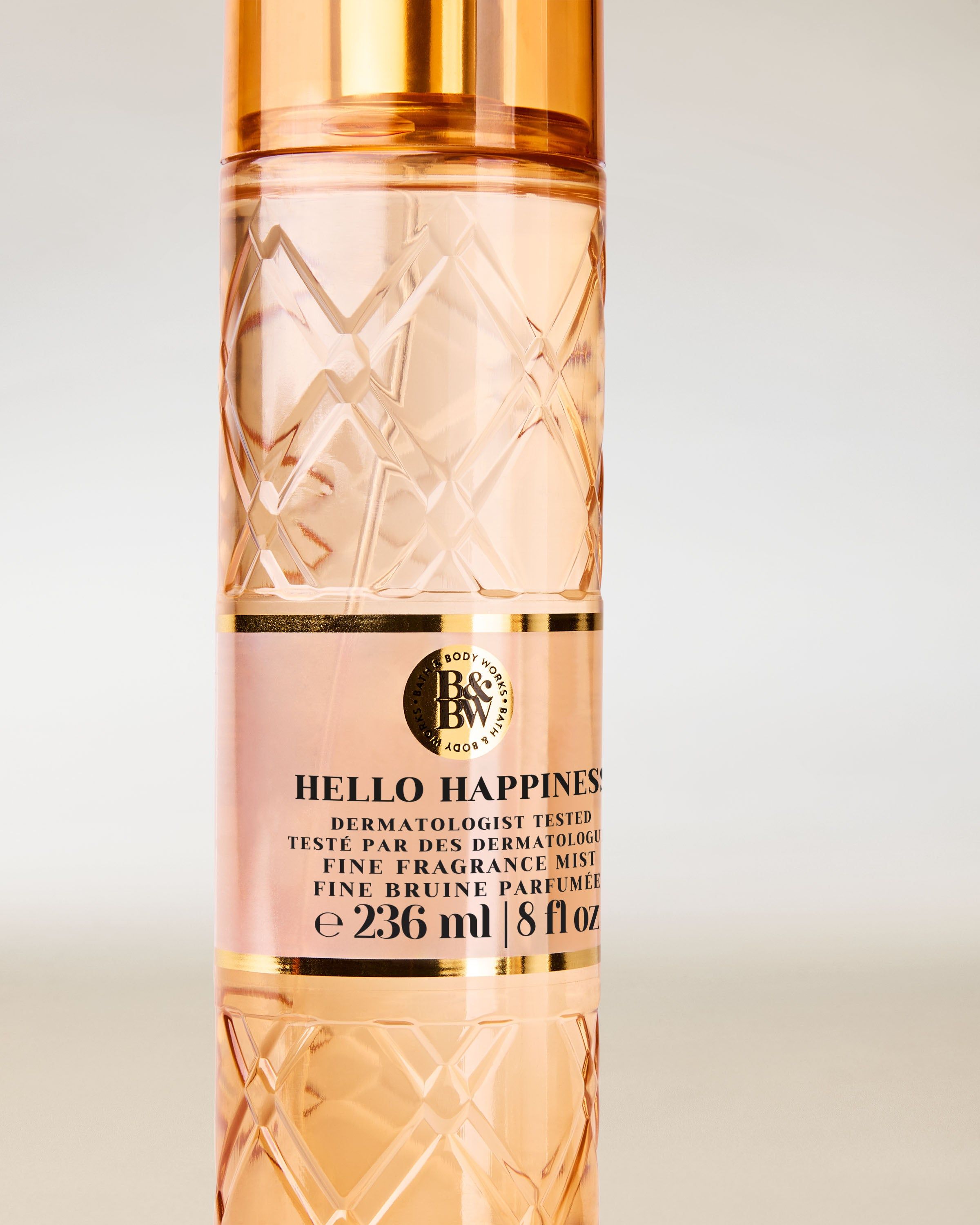 Bath & Body Works Hello Happiness – broskvová voňavá mlha v reliéfní lahvi se zlatým rozprašovačem.