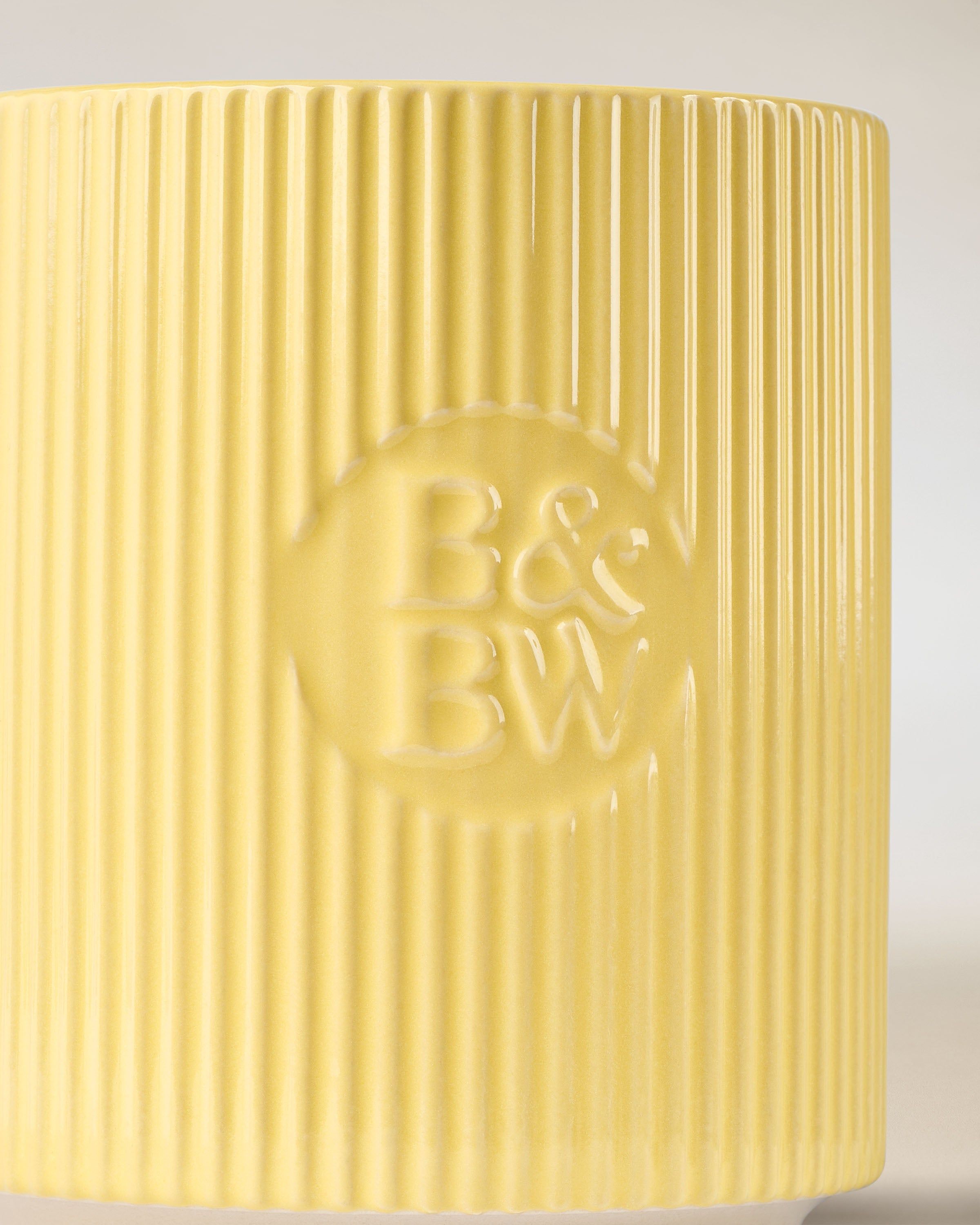 Svíčka Bath & Body Works v žlutém keramickém držáku s rýhovaným povrchem.