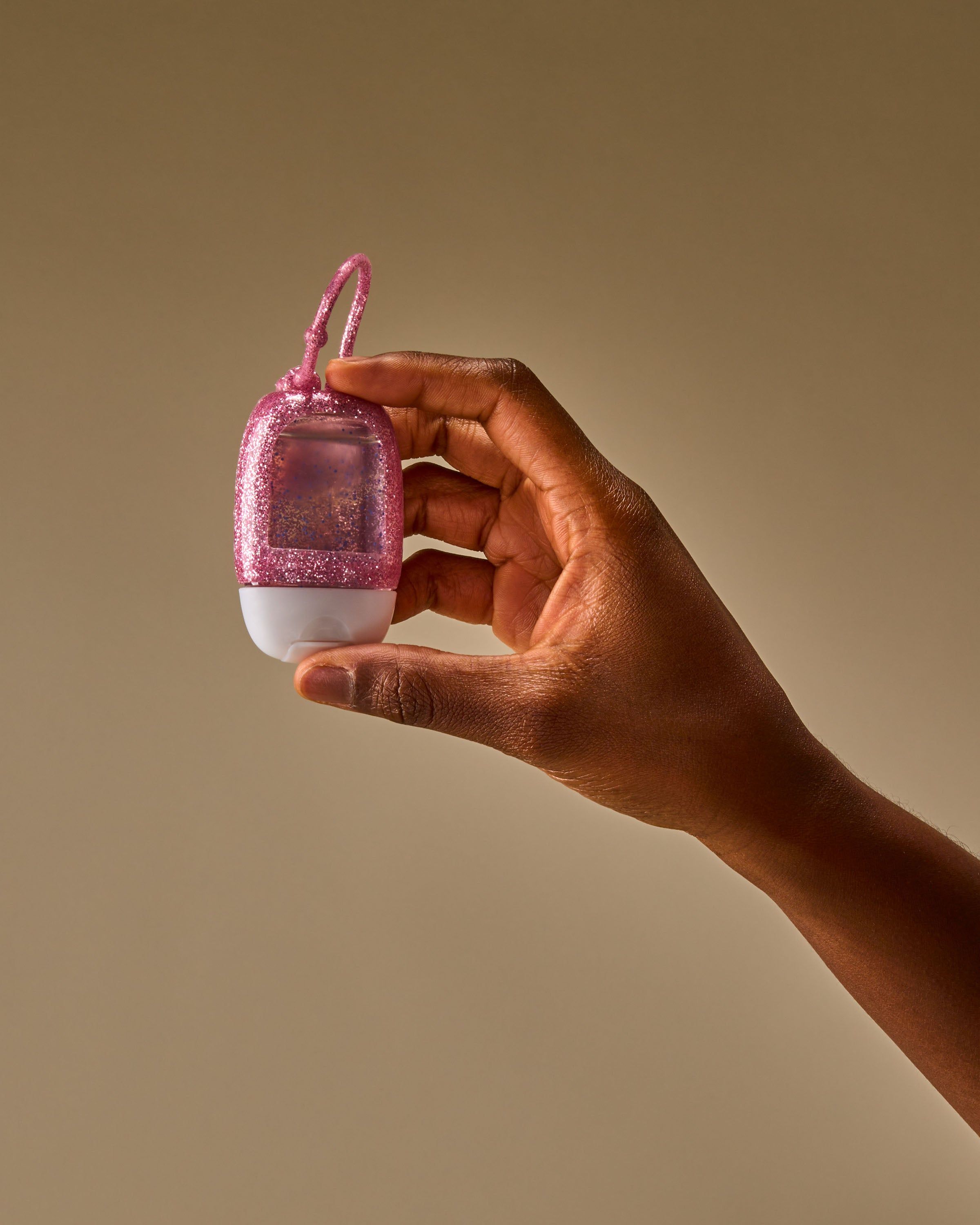 Záběr na třpytivý držák PocketBac držený v ruce, zdůrazňující kompaktní tvar a pružné poutko pro uchycení.