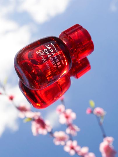 Červená parfémová voda Bath & Body Works Japanese Cherry Blossom na pozadí oblohy a květů