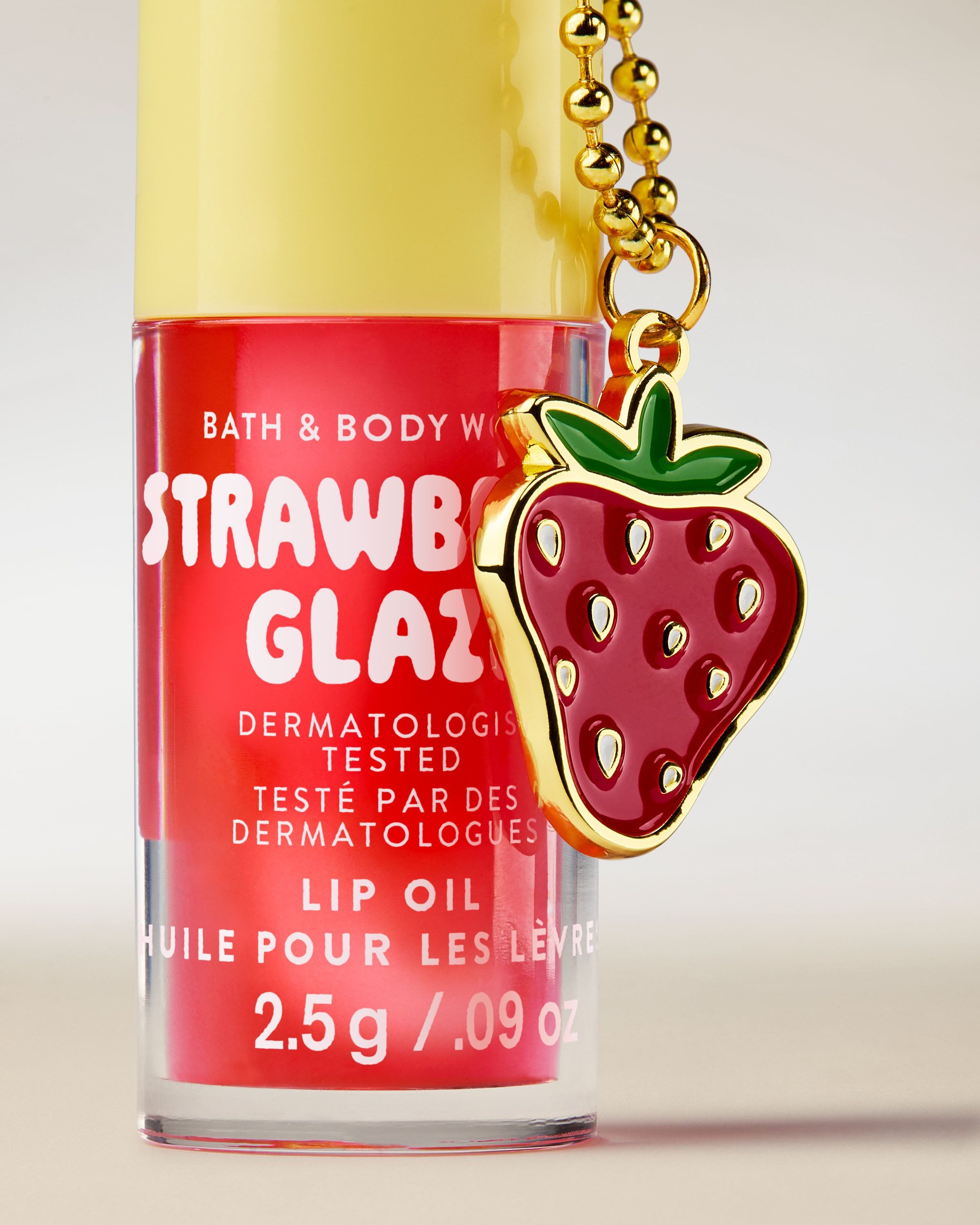Olej na rty Bath & Body Works Strawberry Glaze 2,5 g v růžovém obalu s přívěskem ve tvaru jahody.