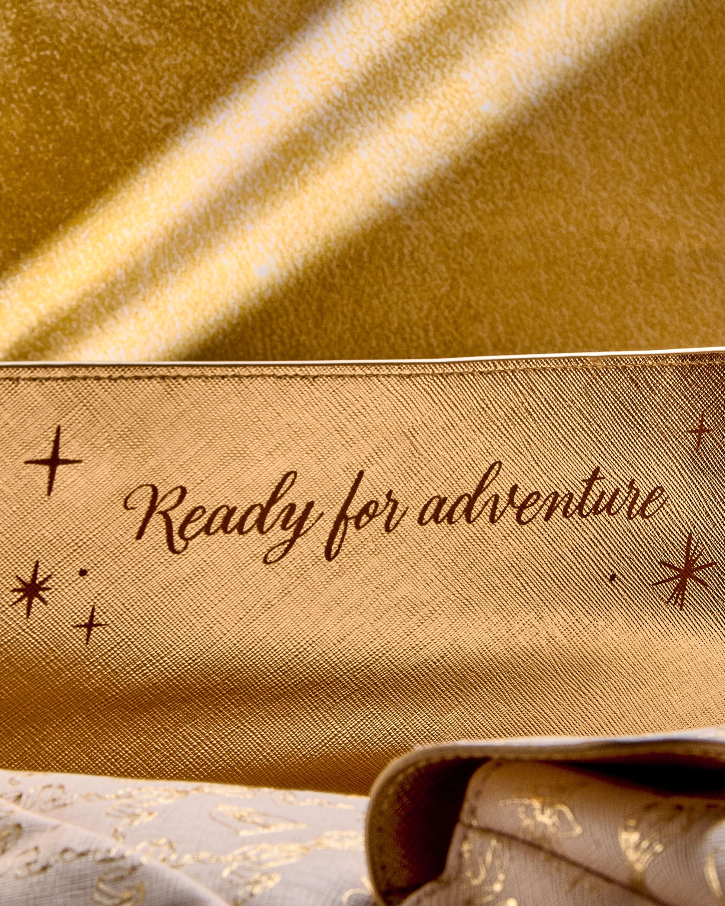 Detail zlatého prvku na krabičce Disney Princess s nápisem „Ready for adventure”.