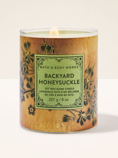 Zapálená svíčka „Backyard Honeysuckle“ ve skle s rostlinným motivem.