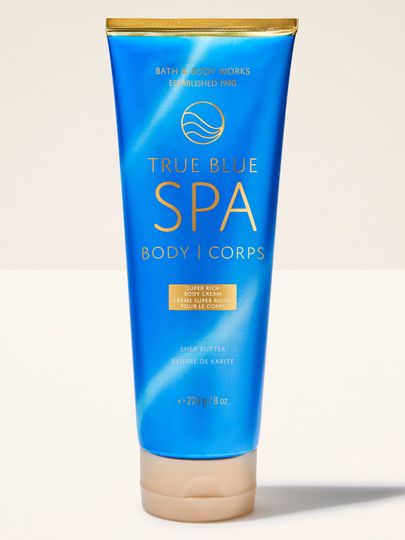 Tělový krém Bath&Body Works True Blue Spa. Modrá tuba se zlatým pruhem a béžovým uzávěrem, s nápisy.
