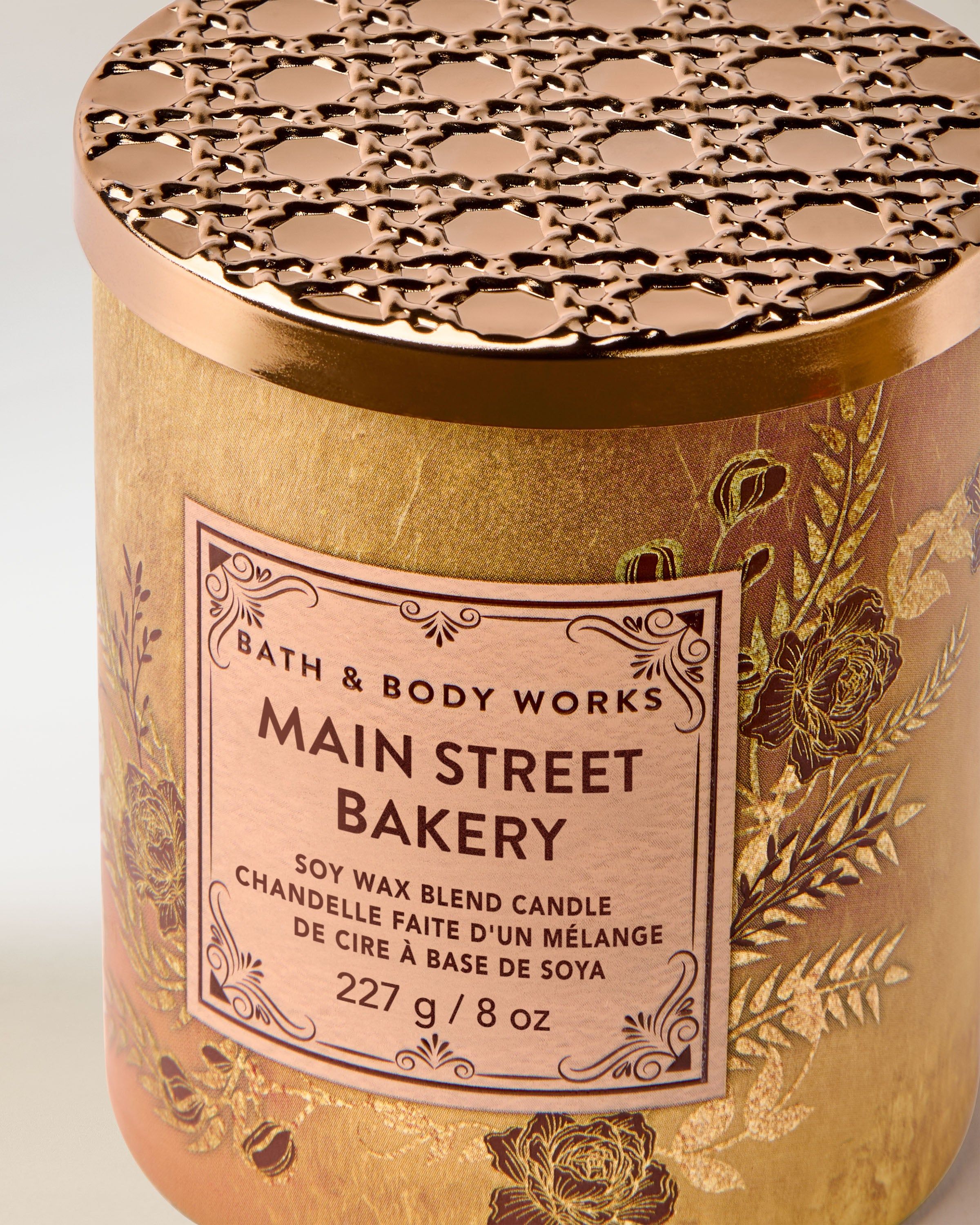 Bath & Body Works Main Street Bakery – svíčka 227 g ve zlatém obalu s rostlinným reliéfem a dekorativním kovovým víčkem.