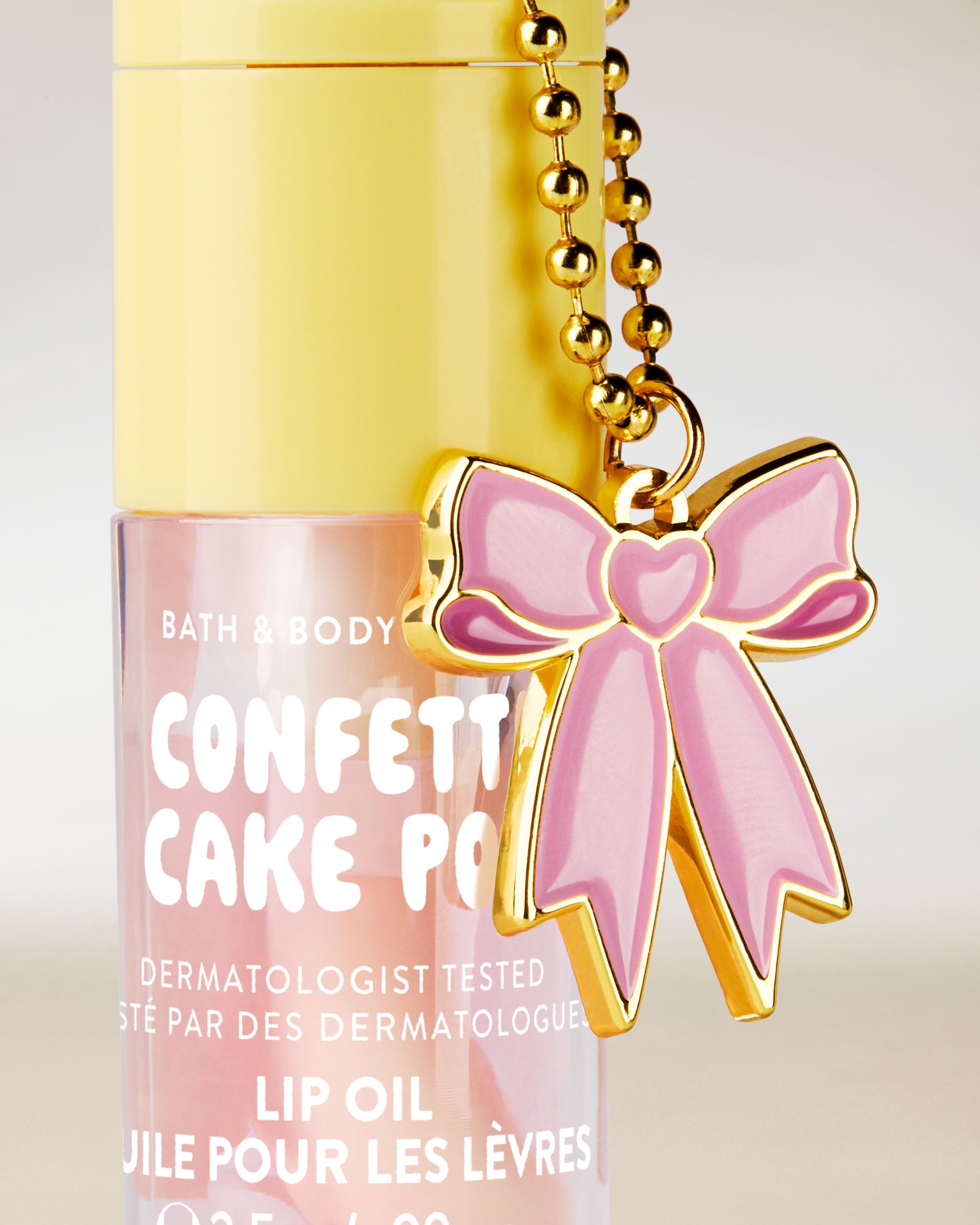 Olej na rty Bath & Body Works Confetti Cake Pop 2,5 g v pastelovém obalu s ozdobným přívěskem mašle.